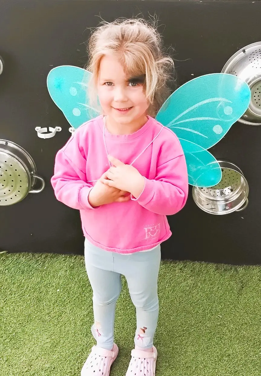 Child in fairy wings playing with bubbles outdoors